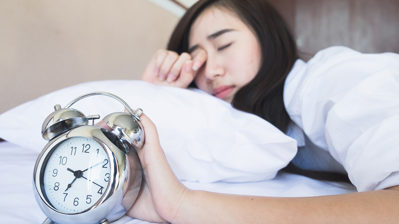 woman waking up from sleeping with alarm clock